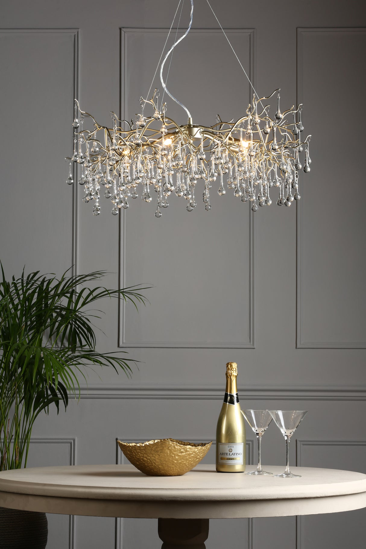 Modern chandelier with crystal droplets above round table with gold bowl, champagne bottle, and two glasses