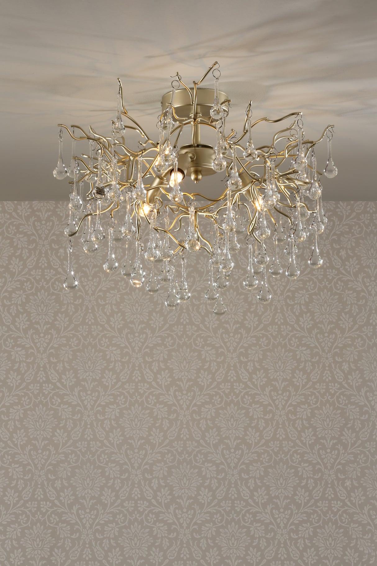 Elegant gold chandelier with hanging glass teardrops against patterned beige wallpaper