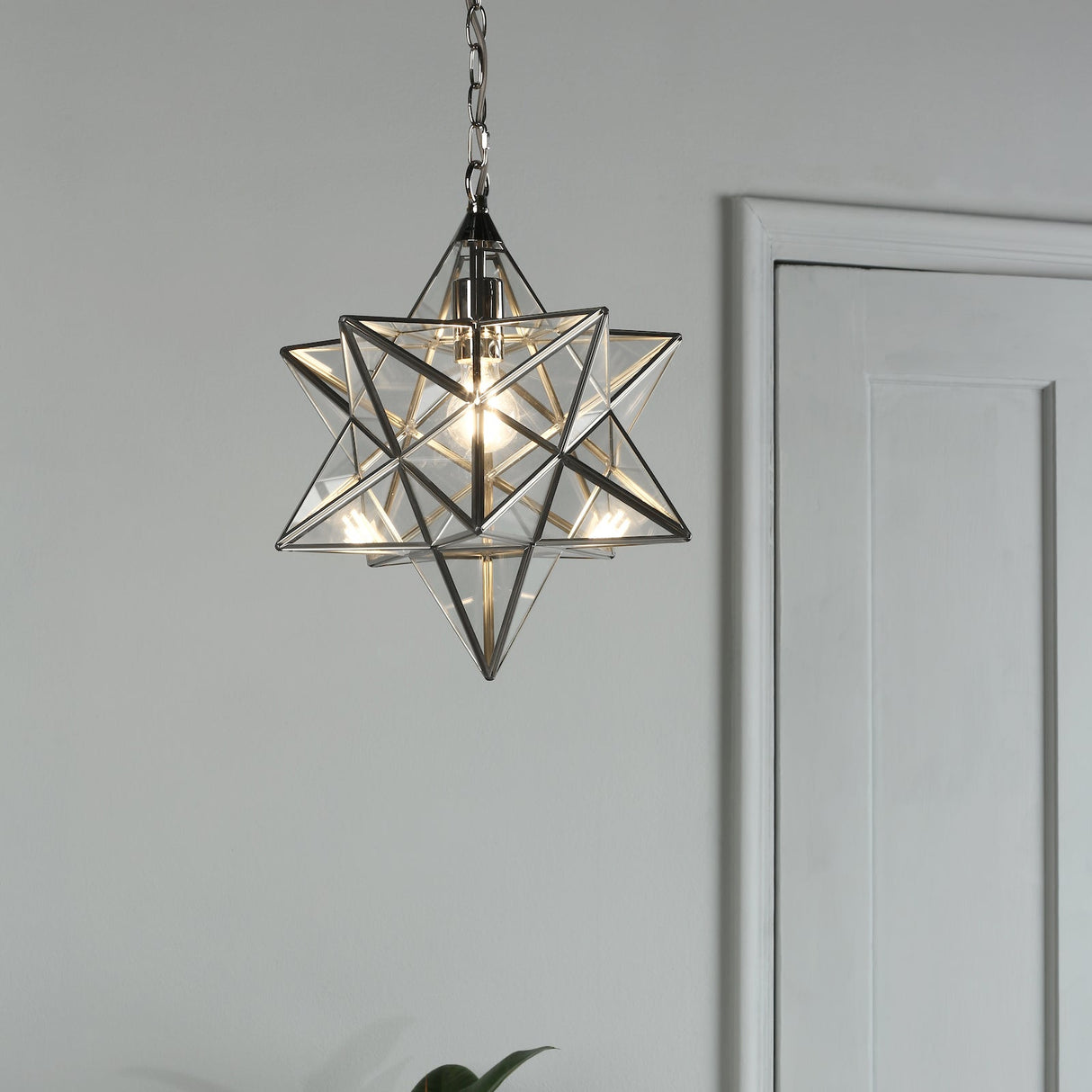 Modern star-shaped geometric pendant light with glass panels hanging near white door