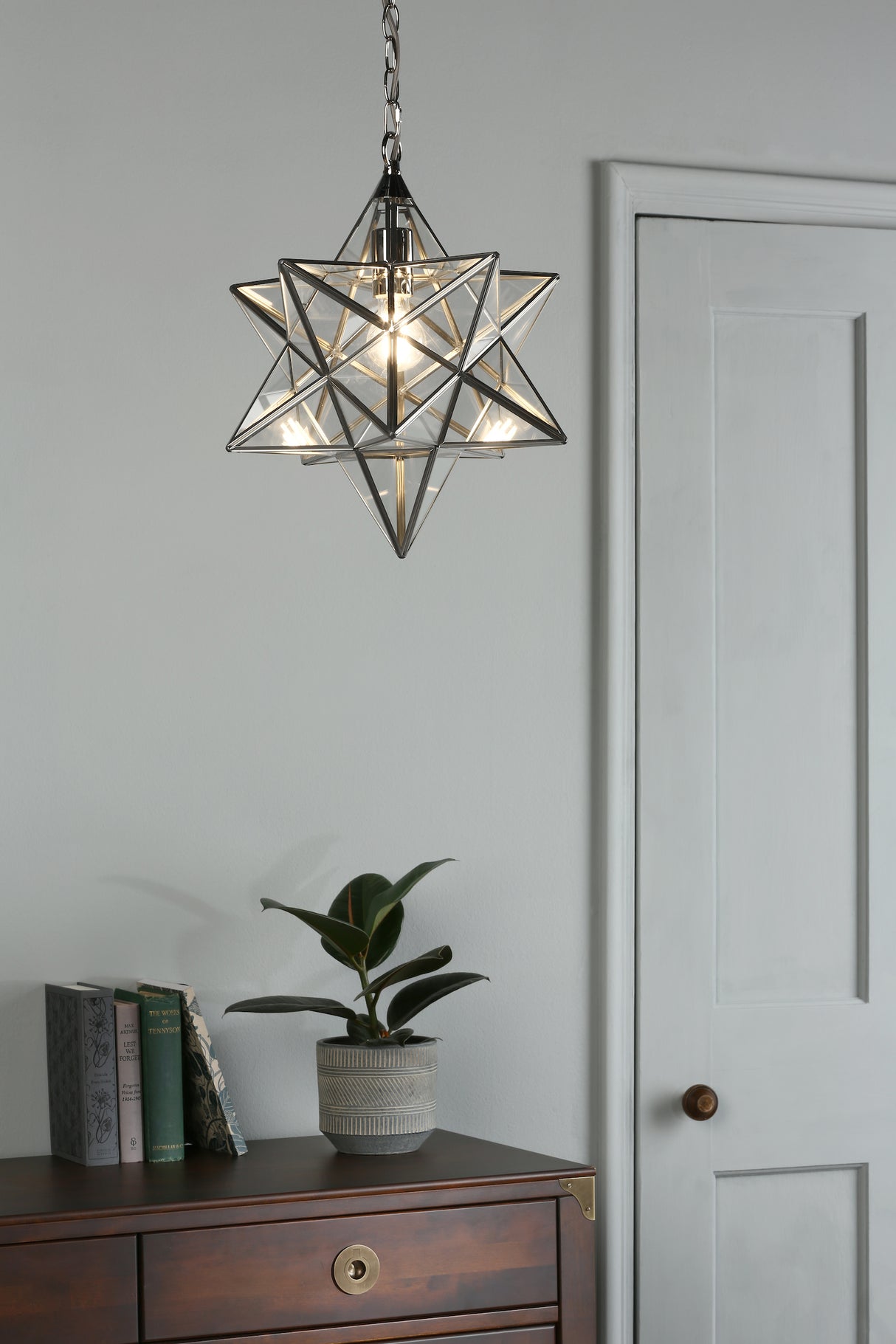 Modern star-shaped glass pendant light over wooden dresser with books and potted plant