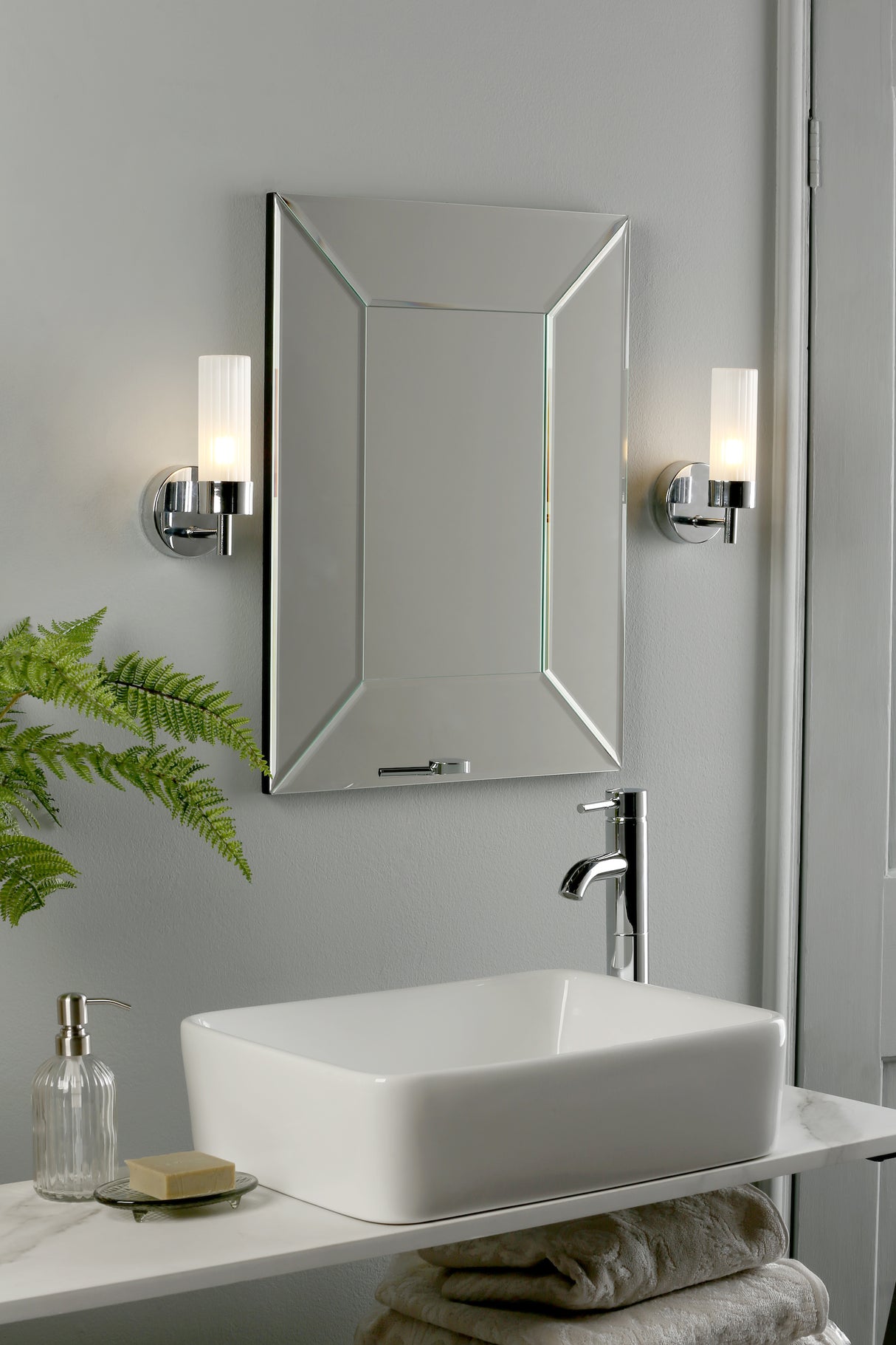 Modern bathroom with rectangular white vessel sink, chrome faucet, frameless mirror, and wall sconces