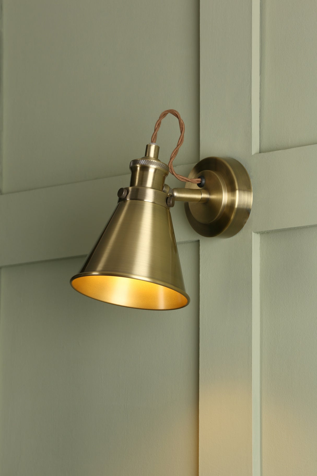 Brushed brass vintage wall sconce light fixture on textured green paneled wall