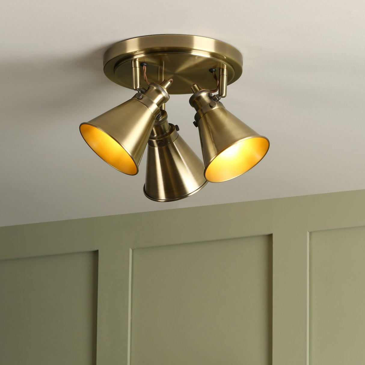 Brass triple spotlight ceiling light mounted on white ceiling above green paneled wall