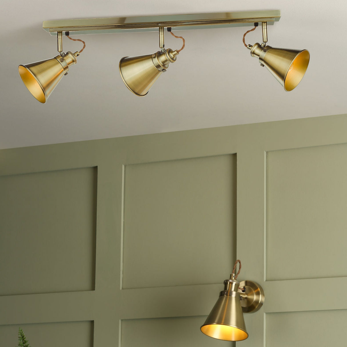 Brass adjustable cone track and wall spotlights mounted on light green paneled wall
