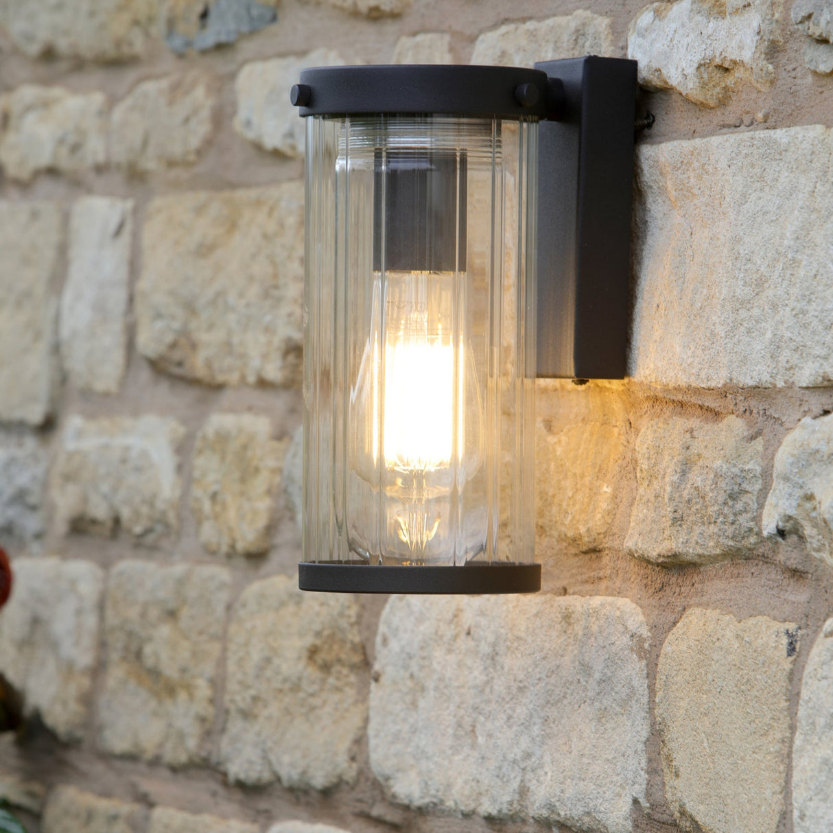Modern outdoor wall light fixture with clear ribbed glass and black metal frame mounted on stone wall