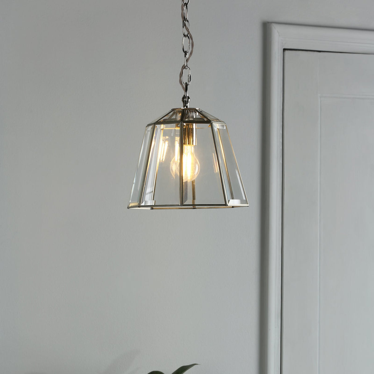 Modern glass pendant light with exposed bulb hanging against gray wall near white door
