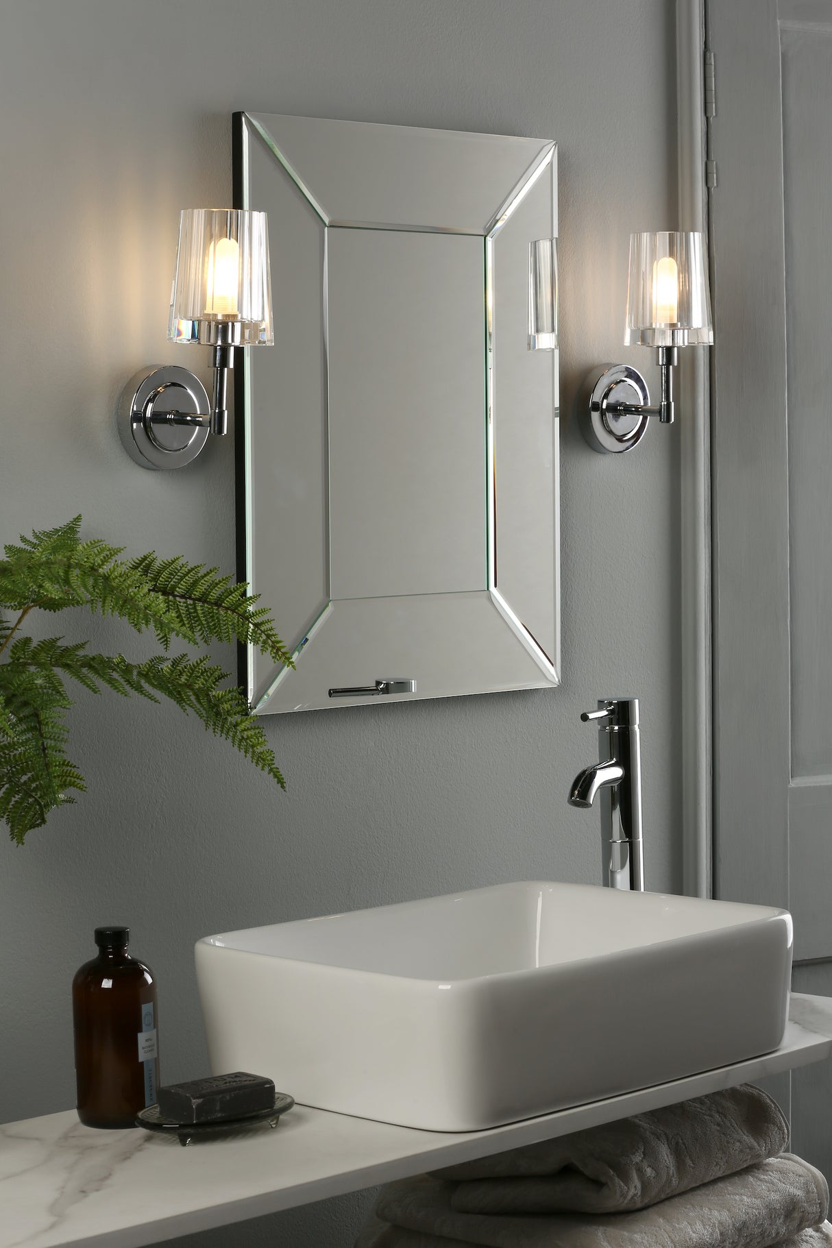 Modern bathroom sink with rectangular white basin, chrome faucet, beveled mirror, and wall sconces