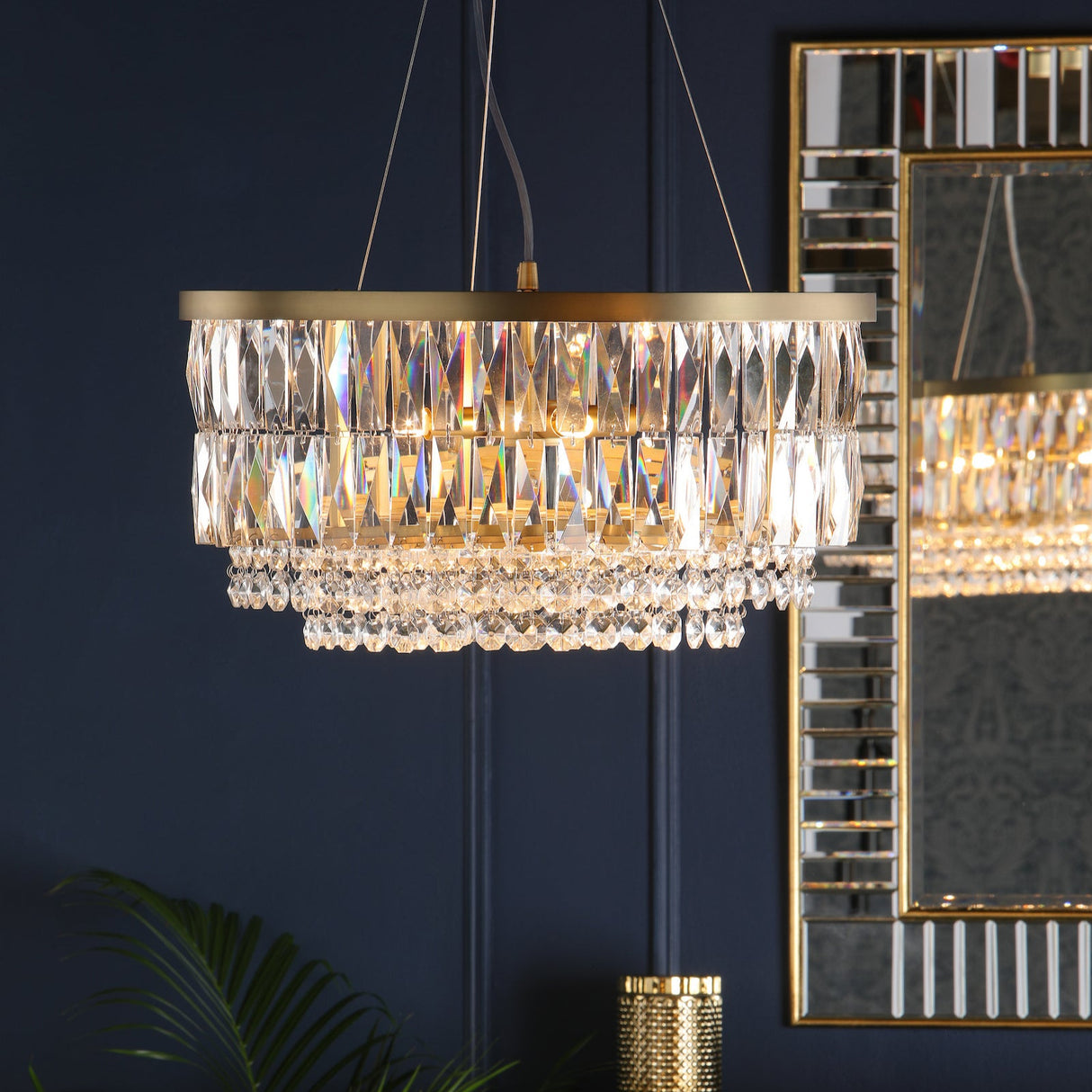 Modern crystal chandelier with gold accents hanging against dark blue wall and mirrored frame