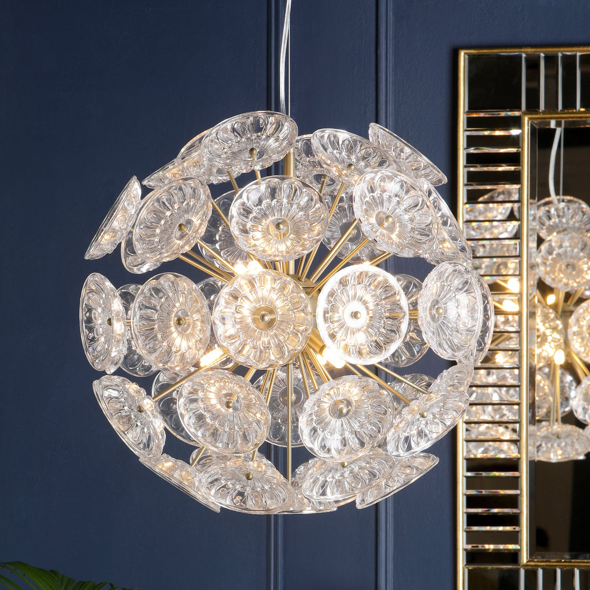 Modern spherical chandelier with clear glass discs and brass rods against navy blue wall