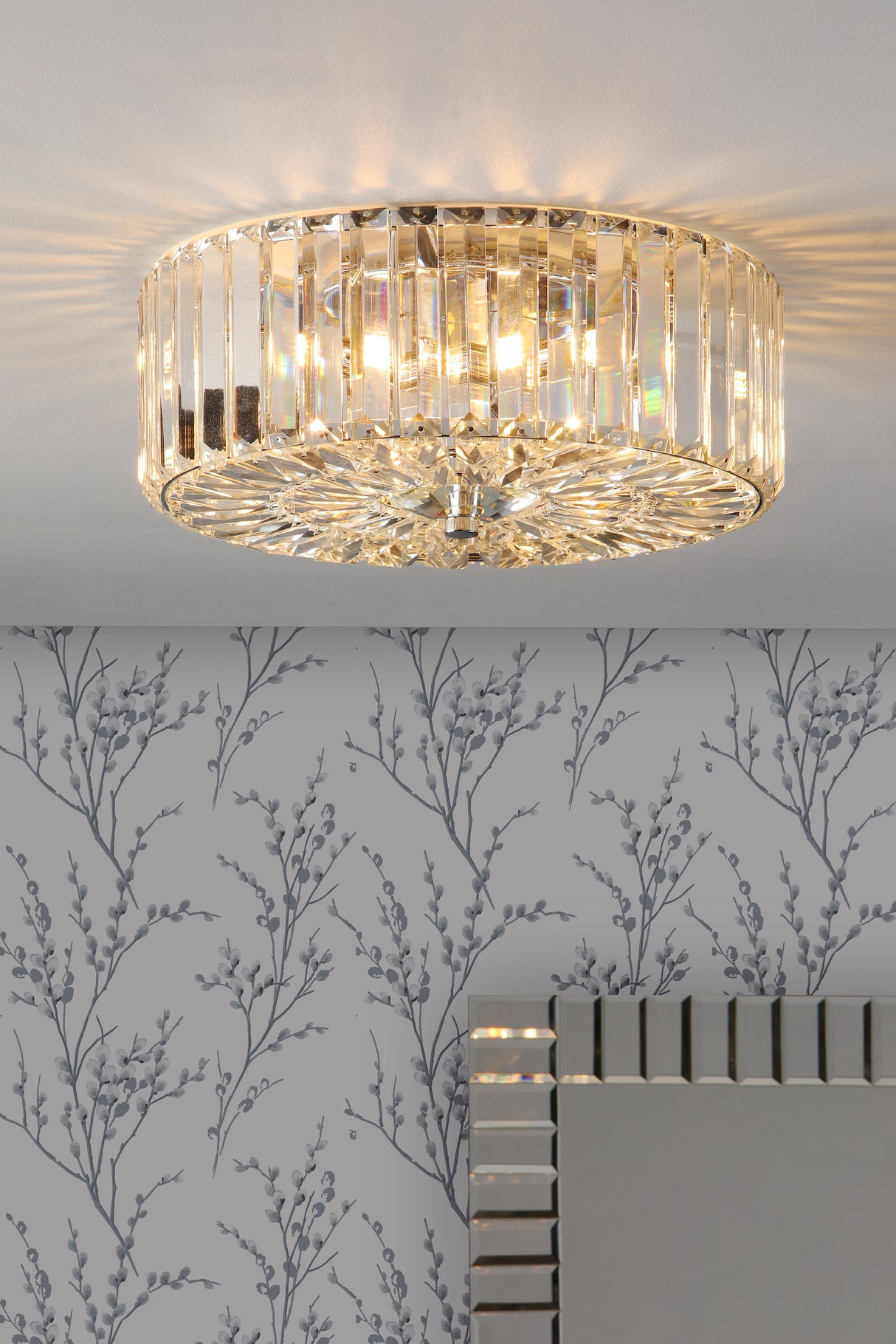 Elegant crystal flush mount ceiling light illuminating floral patterned gray wallpaper and mirrored edge