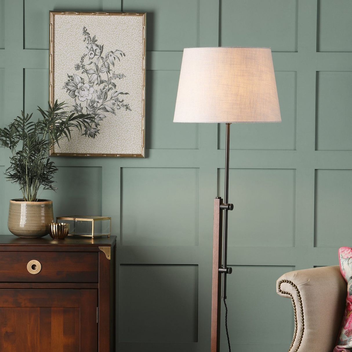 Modern living room corner with green paneled wall, floral artwork, wooden cabinet, potted plant, and floor lamp