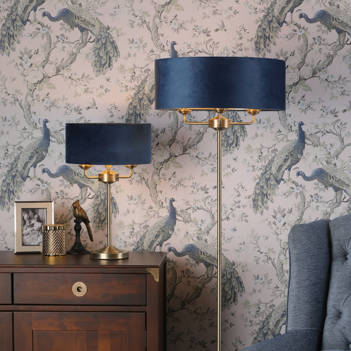 Elegant living room with blue velvet lampshades, brass lamps, wooden sideboard, and peacock wallpaper