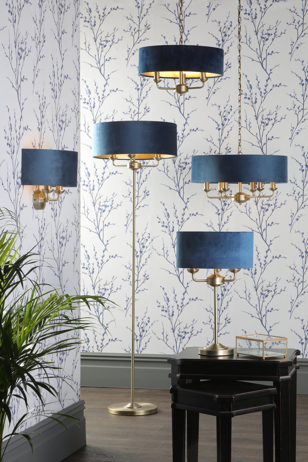 Modern room with blue velvet lampshades on brass floor, table, wall, and hanging lamps against floral wallpaper