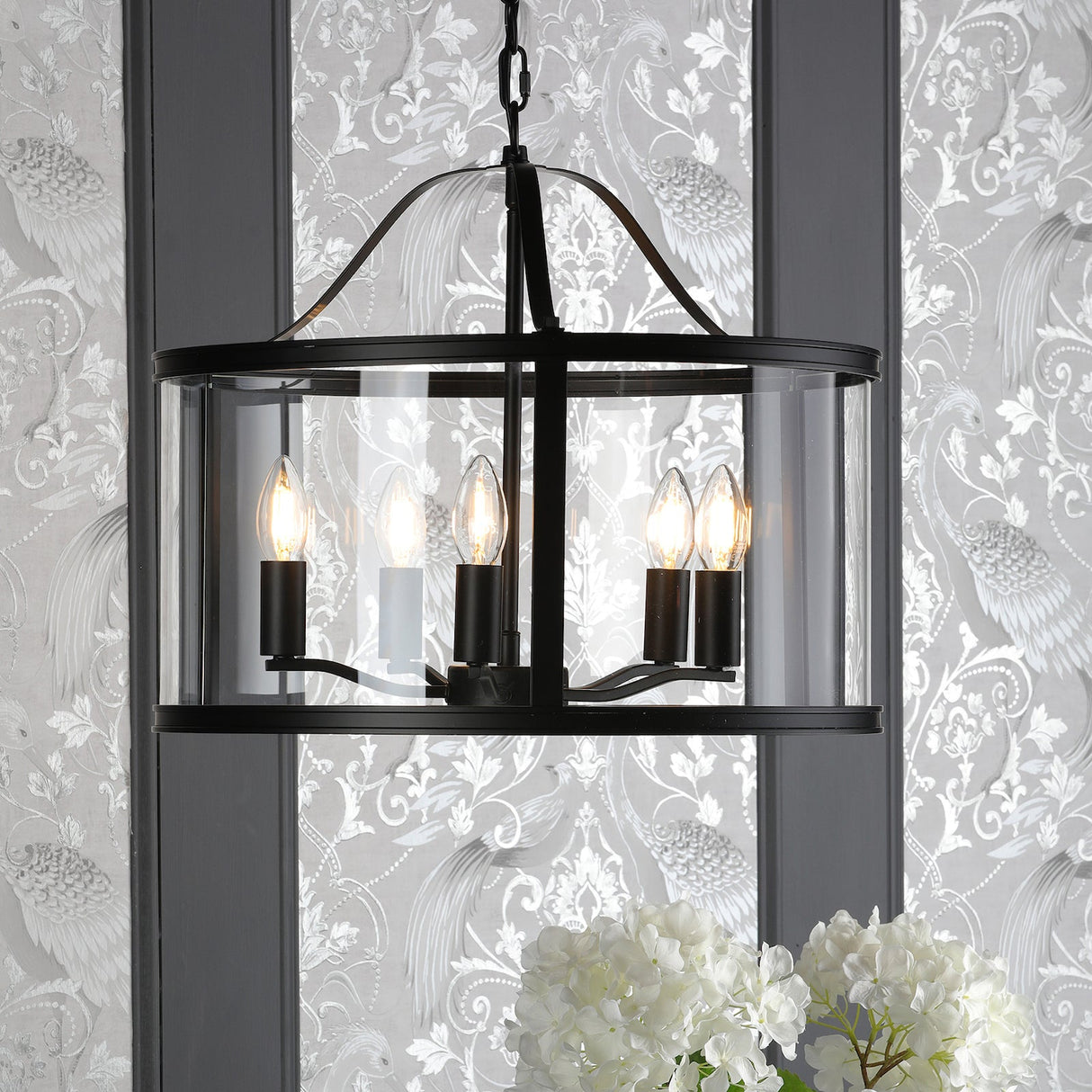 Black metal chandelier with six candle-style bulbs encased in clear glass, hanging in elegant interior