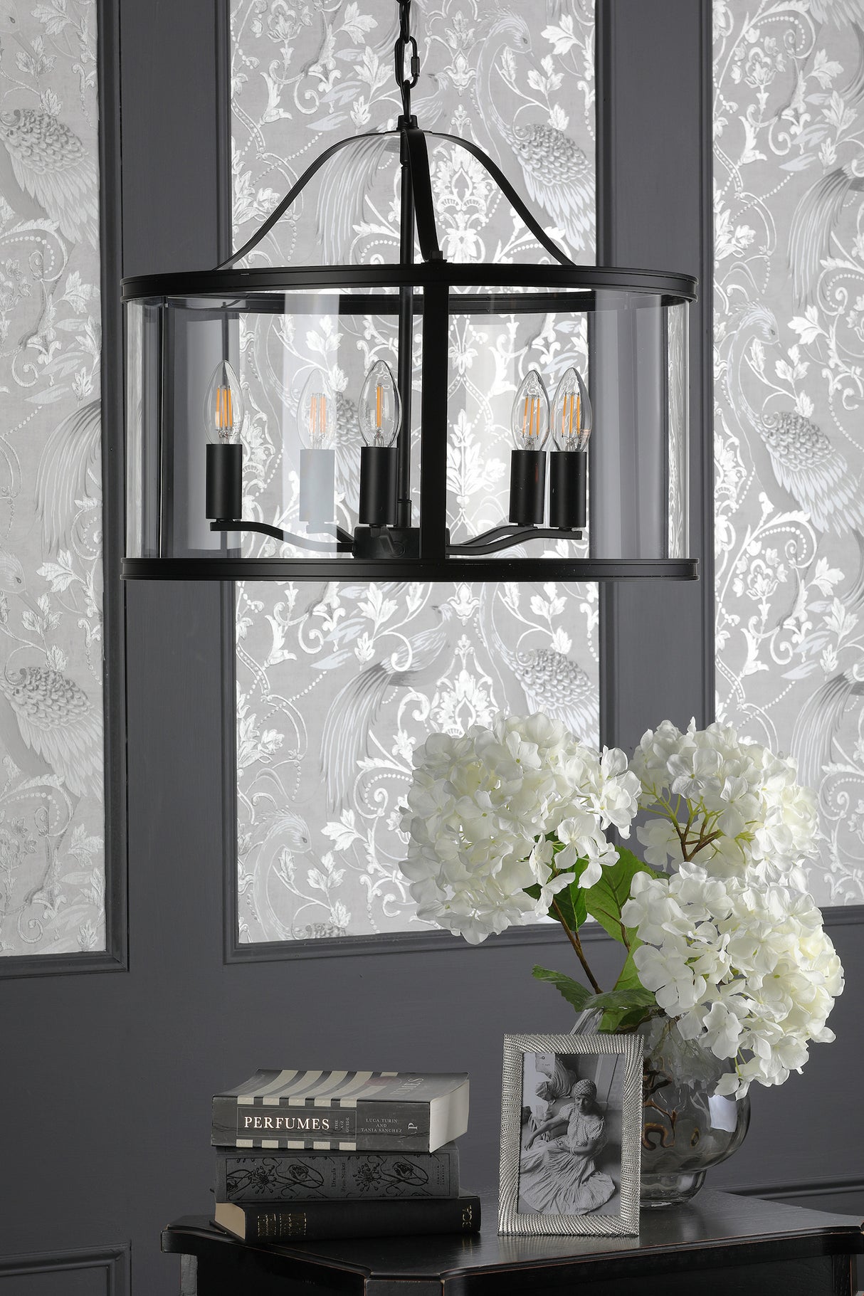Modern black metal chandelier with clear glass shades over table with white hydrangeas, books, and framed photo