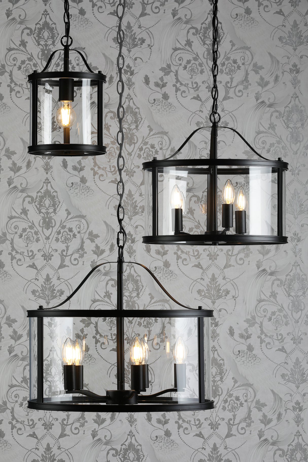 Three black metal and glass pendant lights with Edison bulbs hanging against patterned gray wallpaper