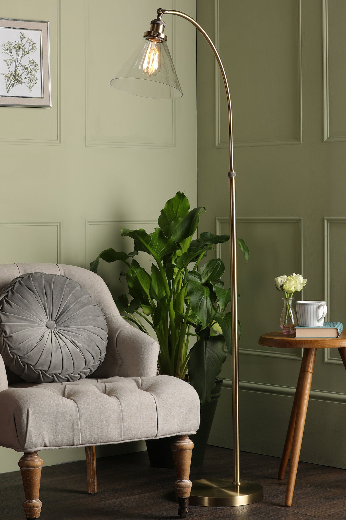 Cozy beige tufted armchair with round gray pillow beside brass floor lamp, green plant, and wooden side table
