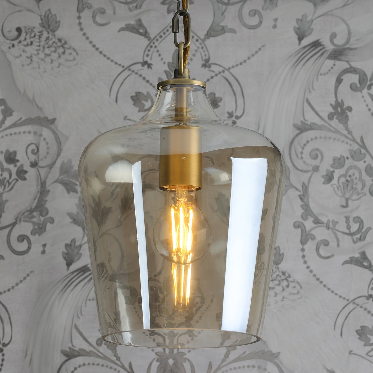 Vintage-style pendant light with amber glass shade and filament bulb against patterned gray wallpaper