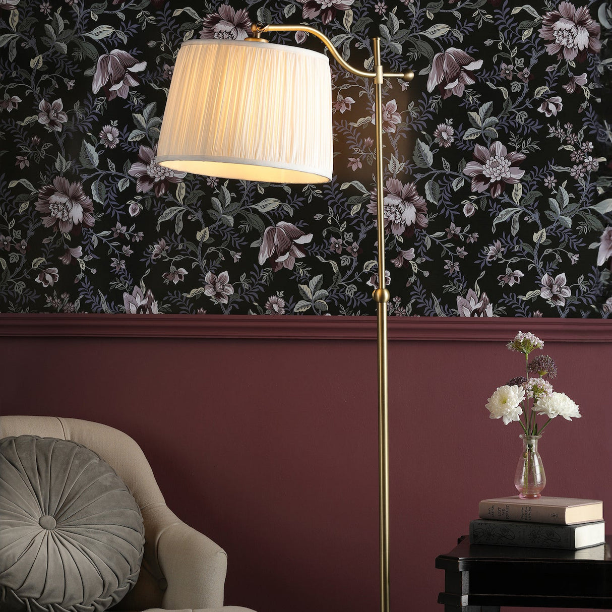 Elegant brass floor lamp with white shade near beige armchair and floral wallpaper in cozy living room