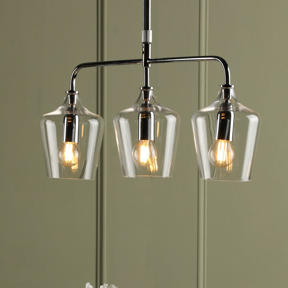 Modern three-light pendant chandelier with clear glass shades and antique bulbs against gray wall