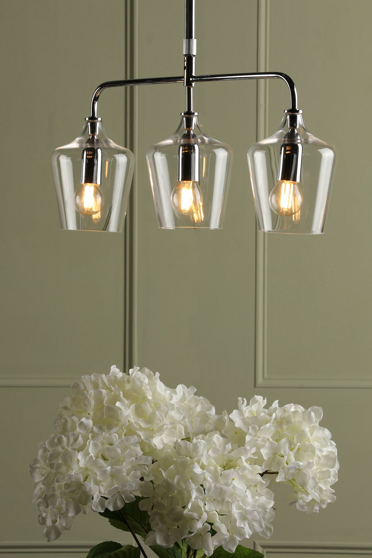 Modern three-light pendant chandelier with clear glass shades above white hydrangea flowers