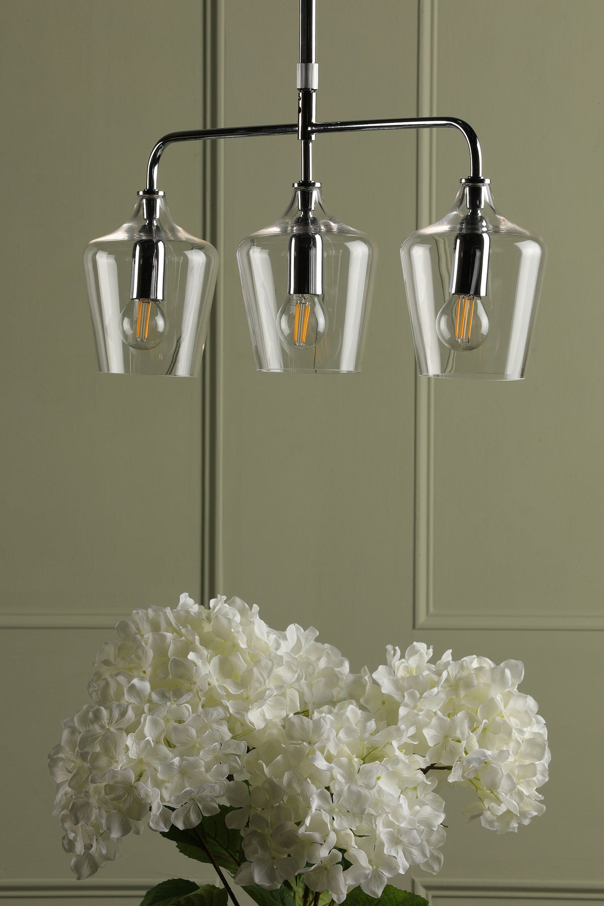 Three-light modern ceiling pendant with clear glass shades above white hydrangea flowers