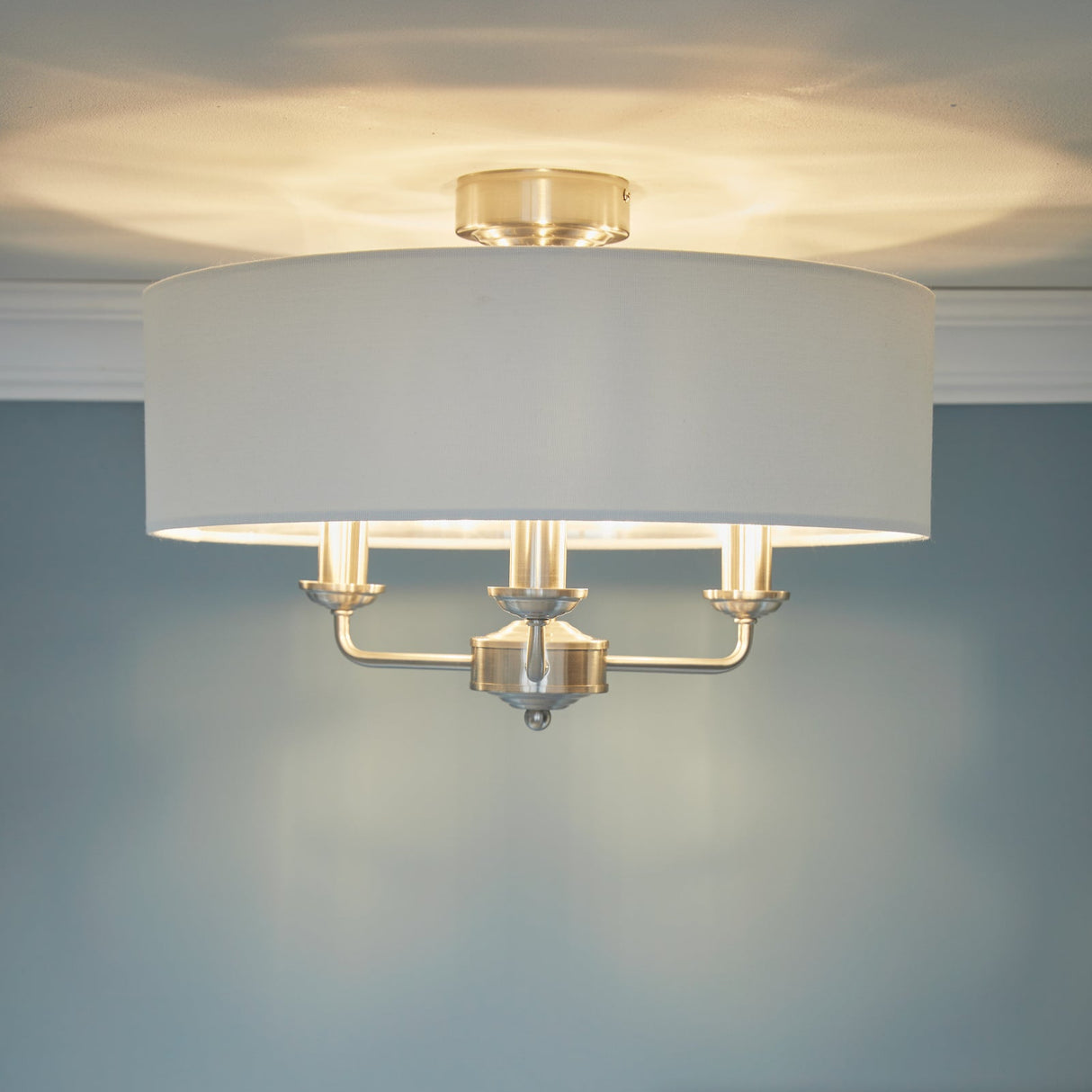 Modern ceiling light fixture with white drum shade and brushed metal arms on blue wall