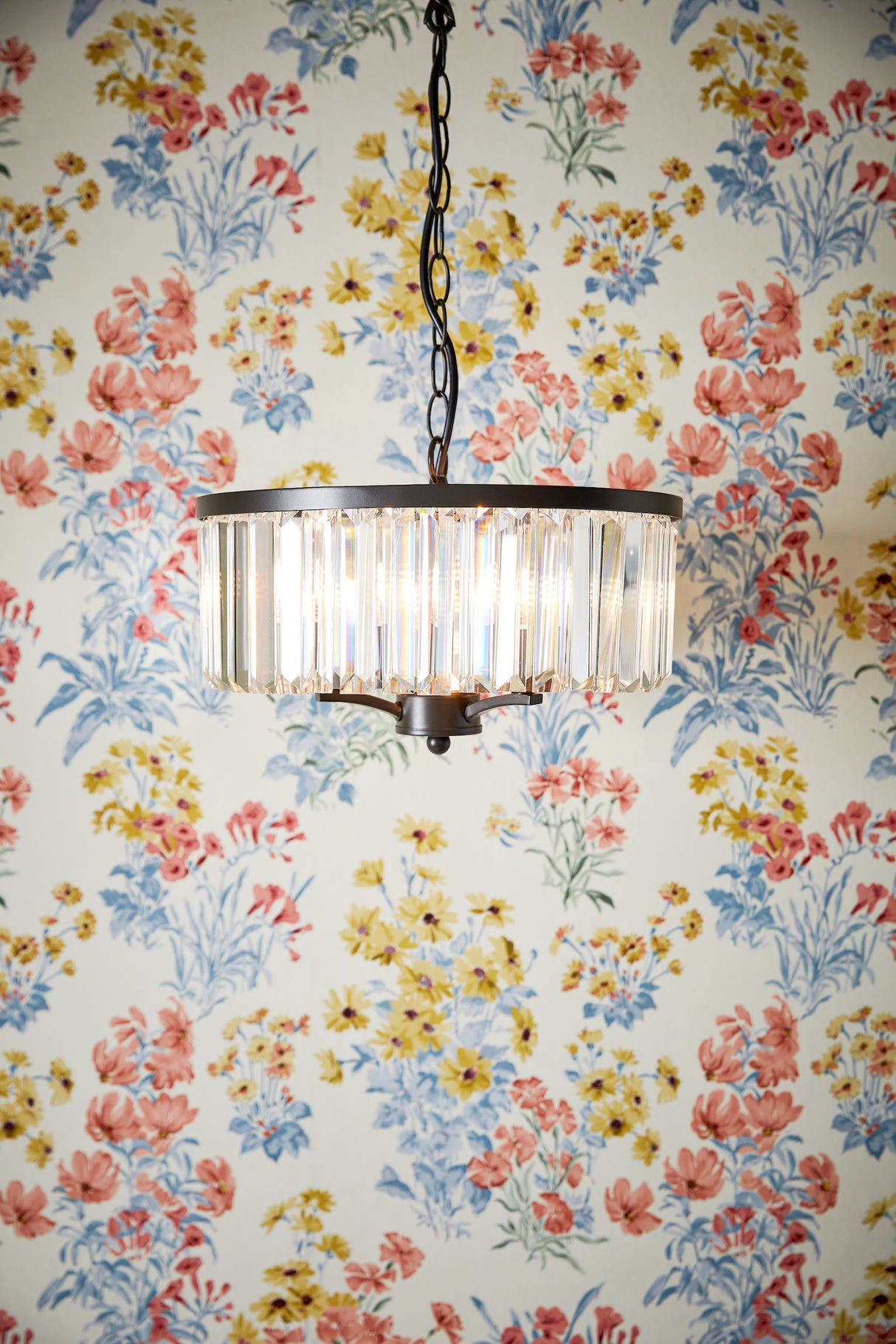 Modern hanging chandelier with vertical glass crystals against floral wallpaper