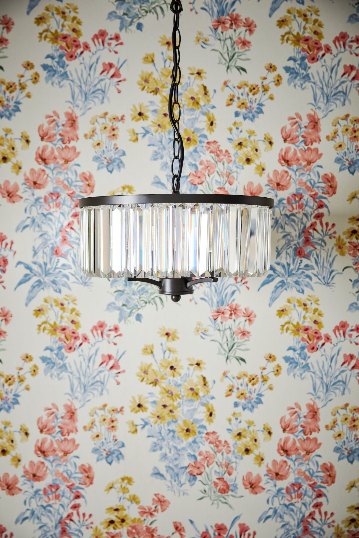 Crystal chandelier pendant light with black metal frame hanging in front of floral wallpaper