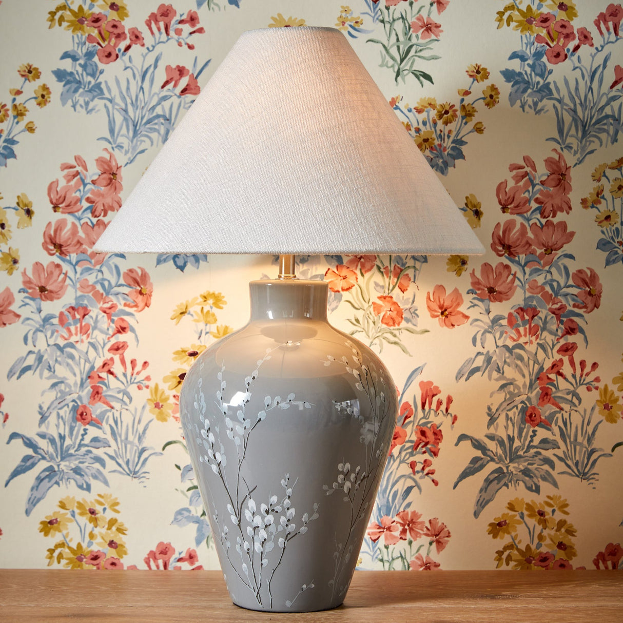 Gray ceramic table lamp with white floral design and cream fabric shade on wooden surface