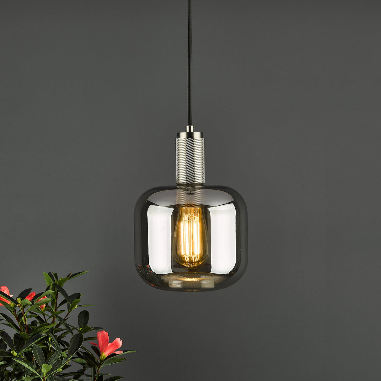 Modern pendant light with amber glass shade and Edison bulb on gray wall with pink flowers