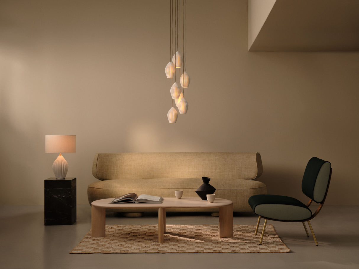 Minimalist living room with beige sofa, black and green lounge chair, wooden coffee table, hanging pendant lights, and table lamp