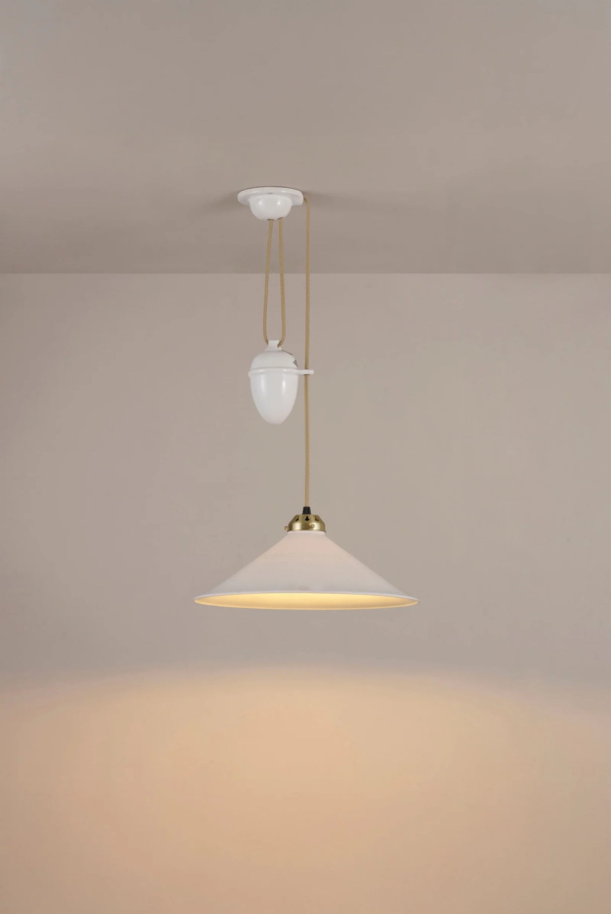 Original BTC Cobb Rise and Fall. Modern pendant light with a beige shade and gold fixture on a plain wall.