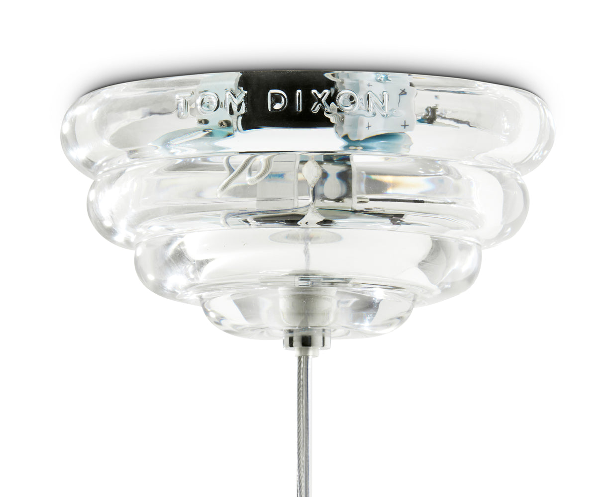Close-up of transparent glass pendant light fixture with metallic cable and Tom Dixon engraving