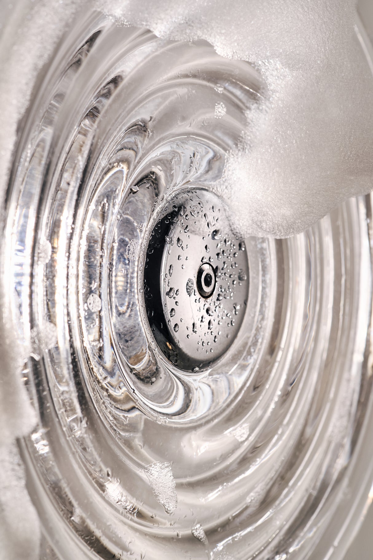 Close-up of clear glass with water droplets and soap foam, highlighting concentric circular patterns
