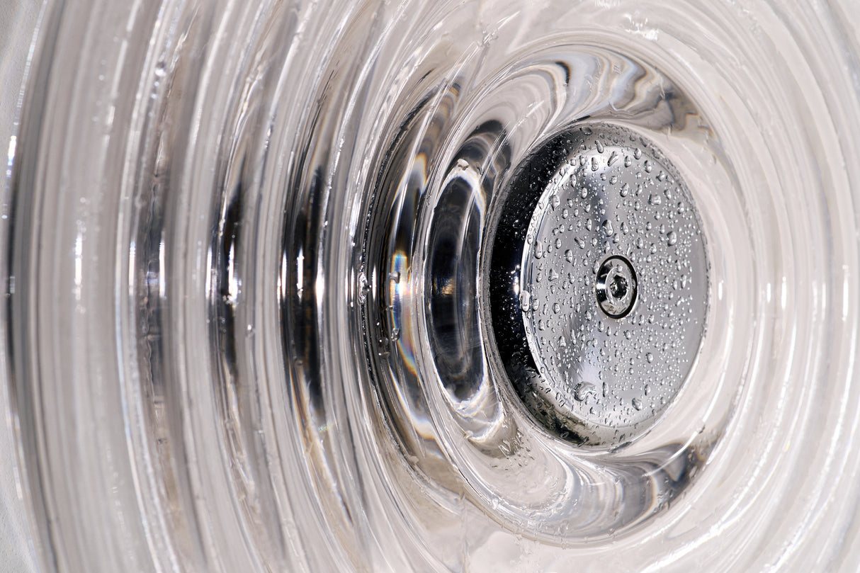 Close-up of a shiny metallic drain stopper with water droplets inside a textured glass basin
