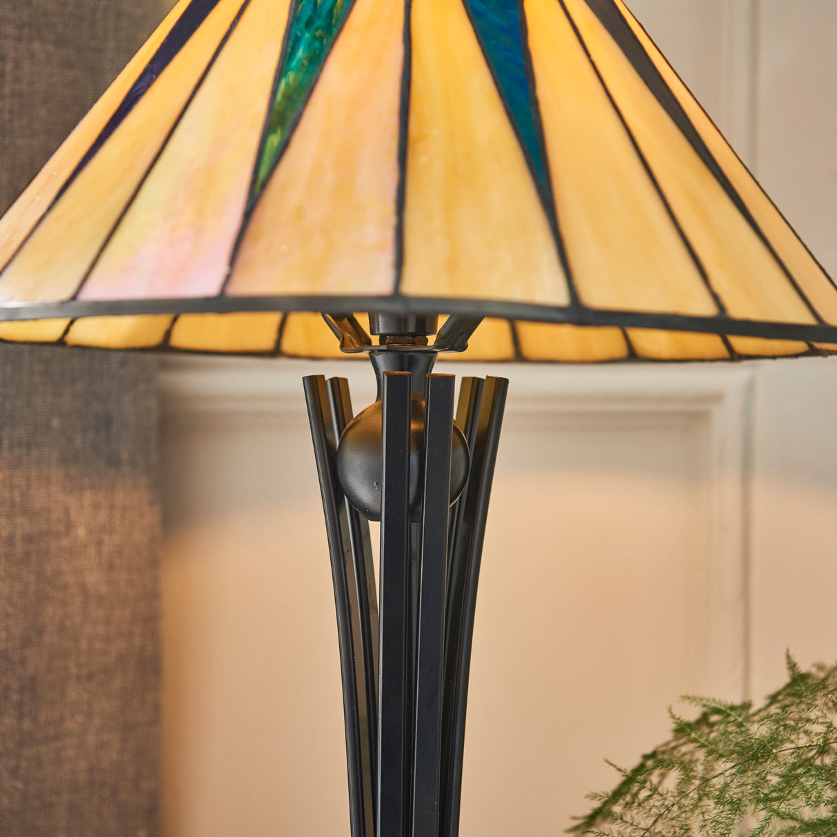 Tiffany-style table lamp with stained glass yellow shade and modern black metal base in cozy room