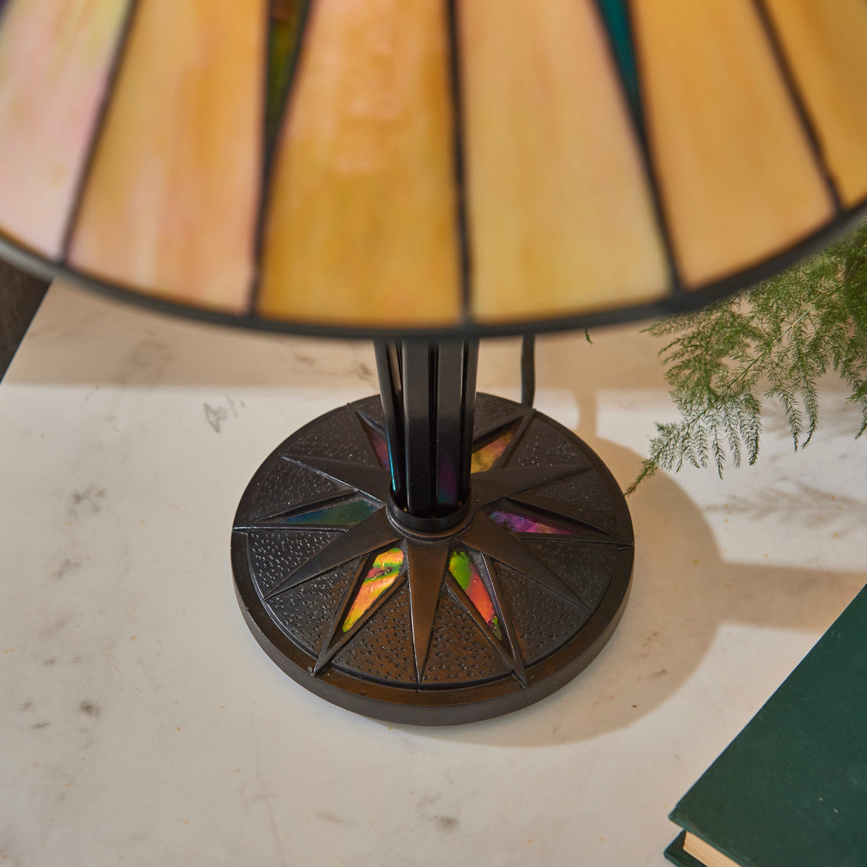 Tiffany-style table lamp with stained glass shade and dark star patterned metal base on marble surface