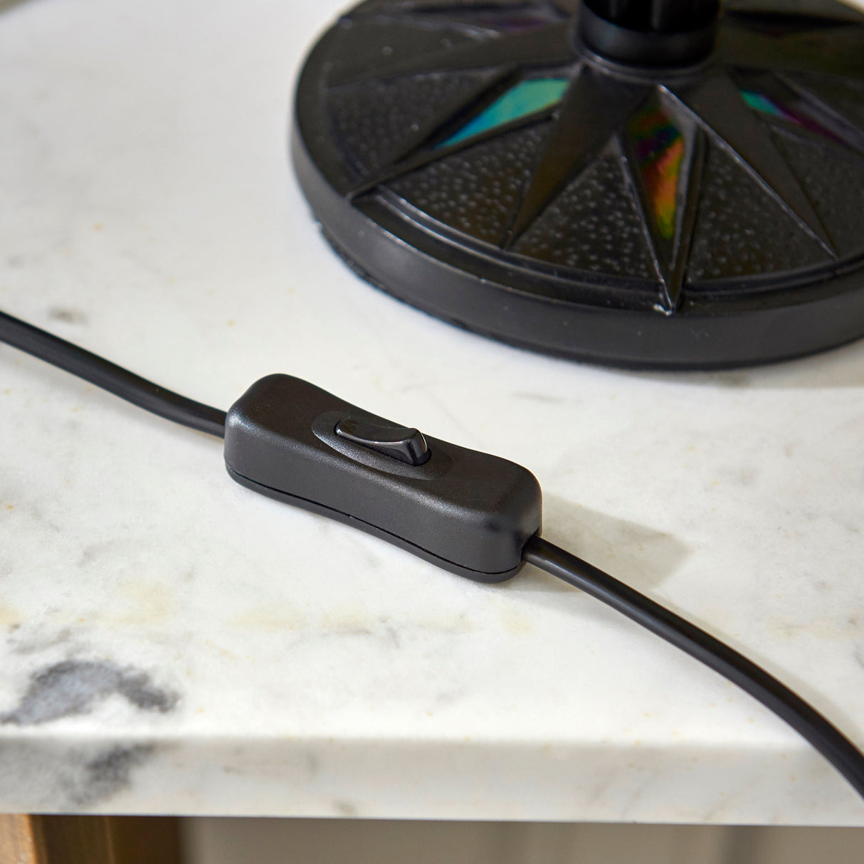 Black inline rocker switch on cord beside textured black lamp base on marble surface
