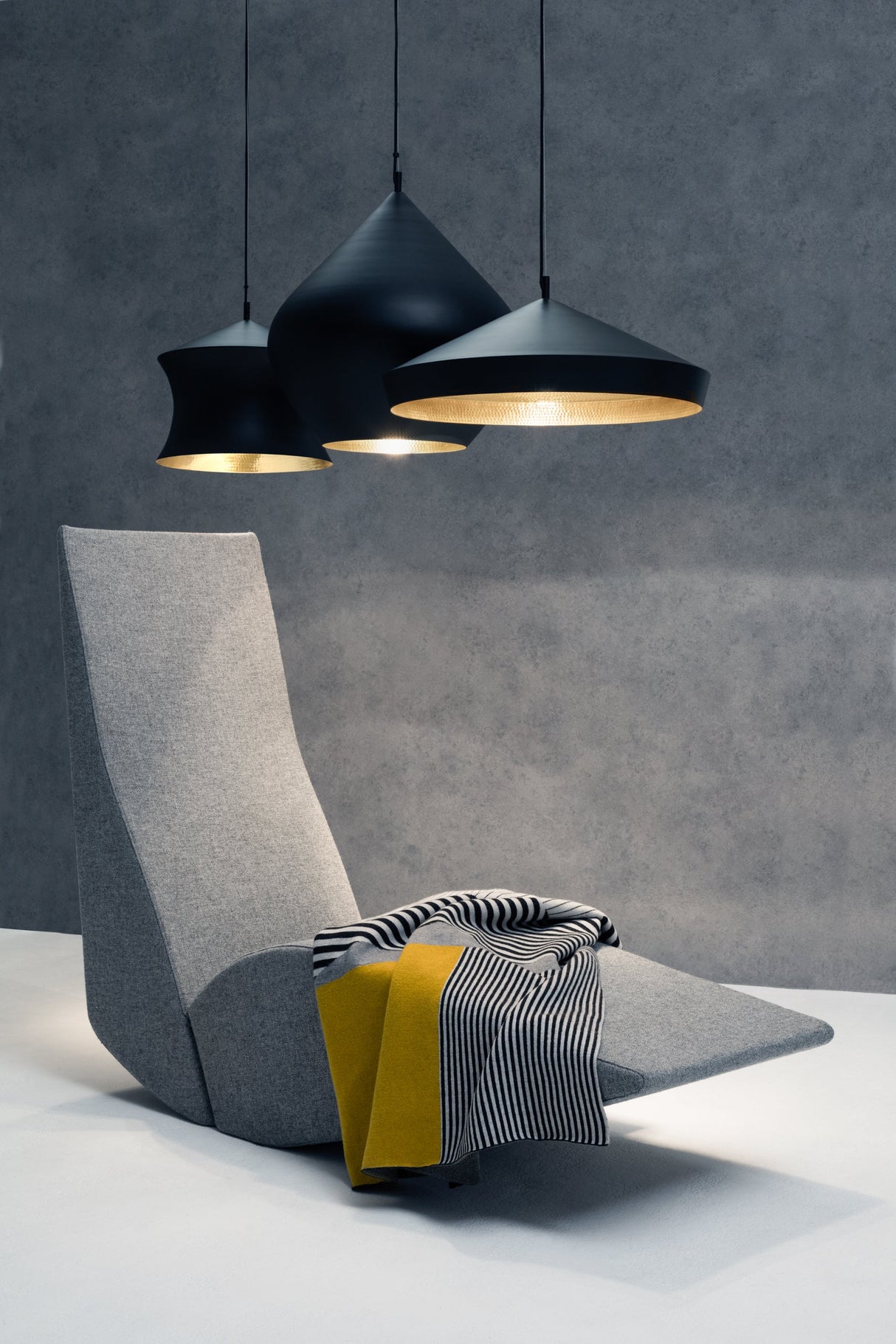 Modern gray lounge chair with striped yellow and black throw blanket under three black pendant lights on gray wall