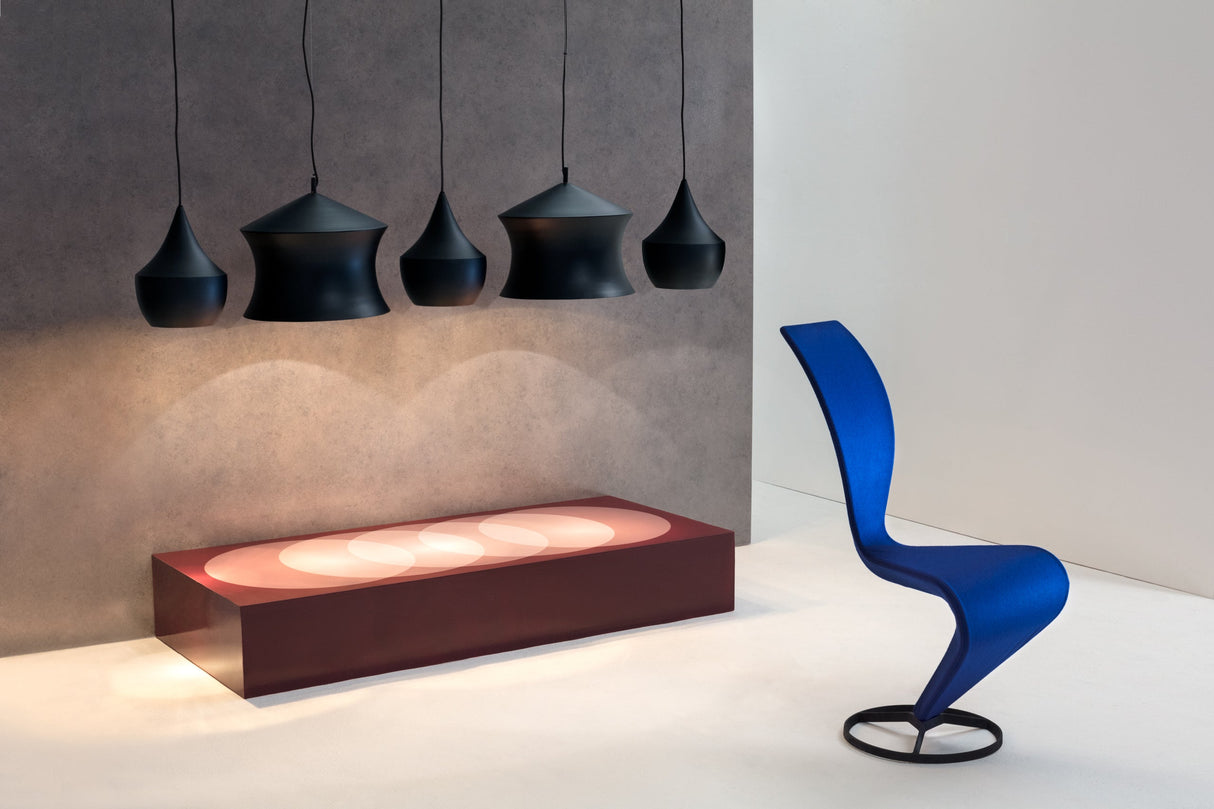 Modern black pendant LED lights hanging over a maroon illuminated bench with a curvy blue chair on white floor