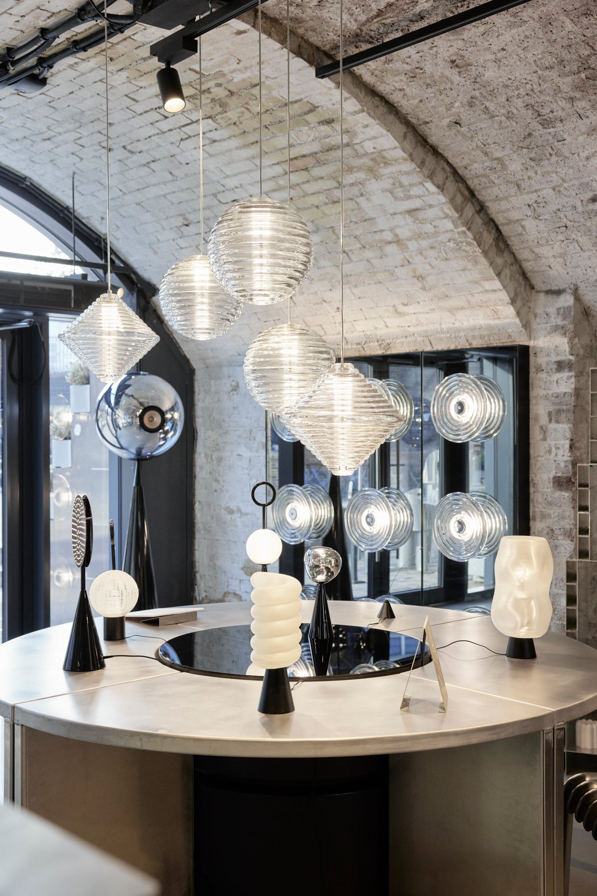 Modern interior with hanging ribbed glass pendant lights and sculptural table lamps on circular metal table under stone arch ceiling