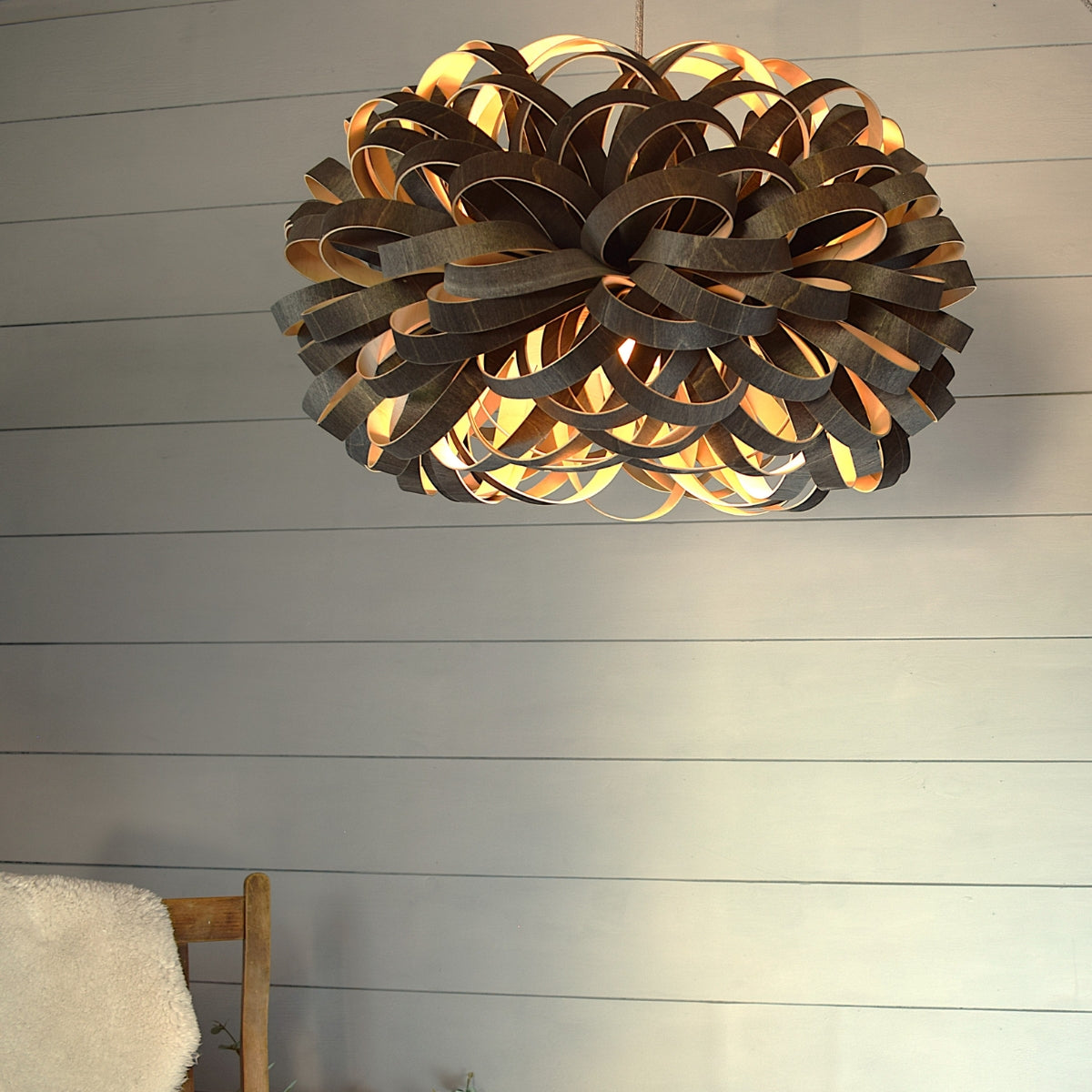 Modern wooden allium pendant light with intricate loops, hanging in minimalist room with wooden chair