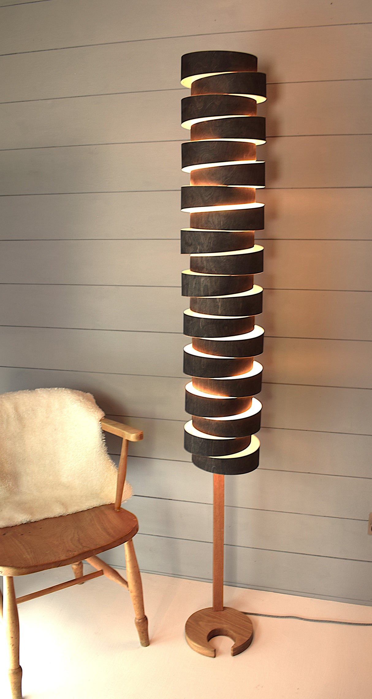 Amos Lighting modern wooden floor lamp with spiral slats next to wooden chair with white fluffy throw