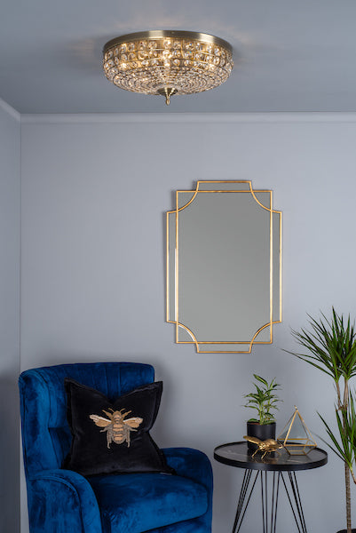 Antique brass flush mount ceiling light with crystals in modern living room featuring blue velvet chair, gold bee pillow, black side table, and gold-trim mirror
