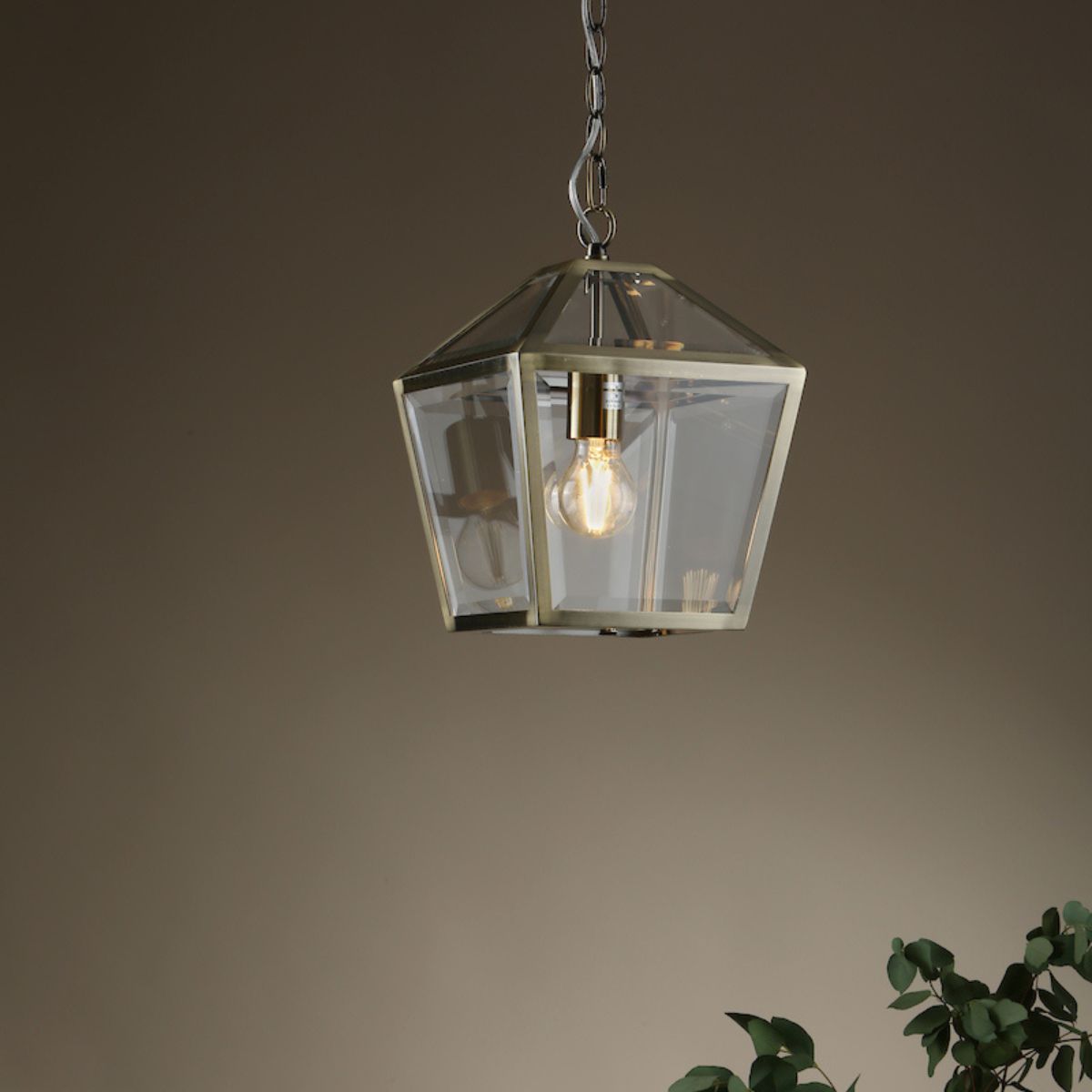 Antique brass lantern pendant light with clear glass panels hanging from chain indoors
