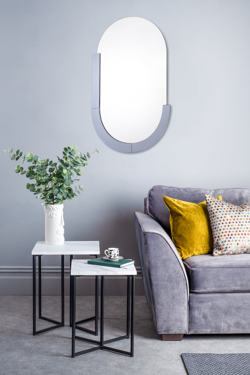 Modern living room with Dar Kaylee oval mirror, gray sofa, yellow and patterned cushions, nesting tables with plant vase