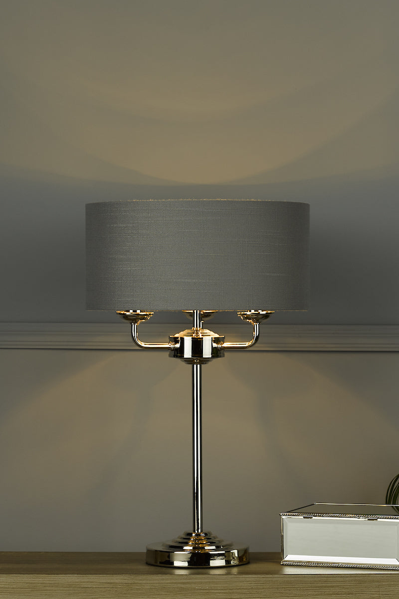 Polished nickel table lamp with charcoal fabric shade on wooden surface next to silver decorative box