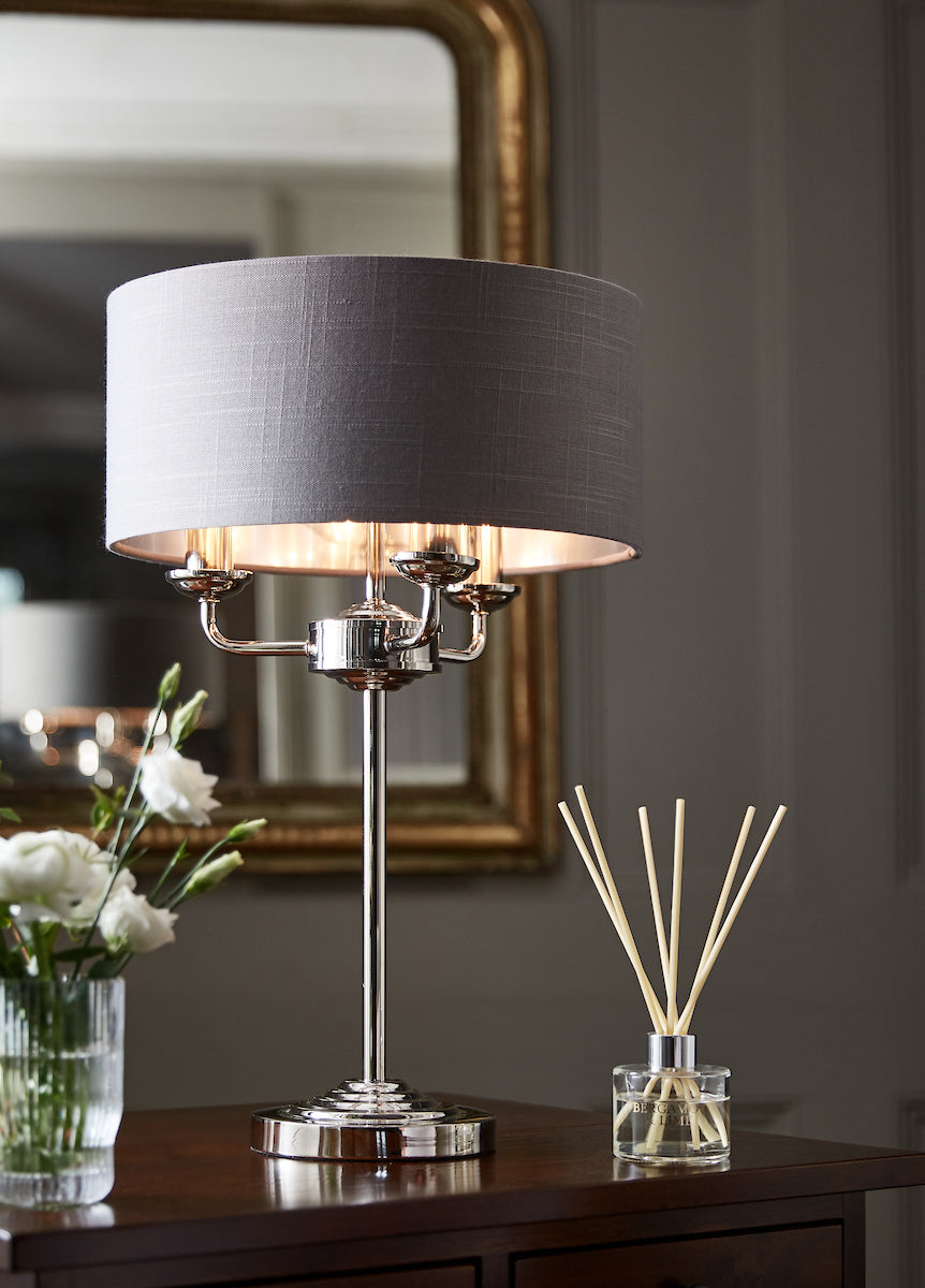 Polished nickel Laura Ashley Sorrento table lamp with charcoal fabric shade on wooden table with flowers and reed diffuser