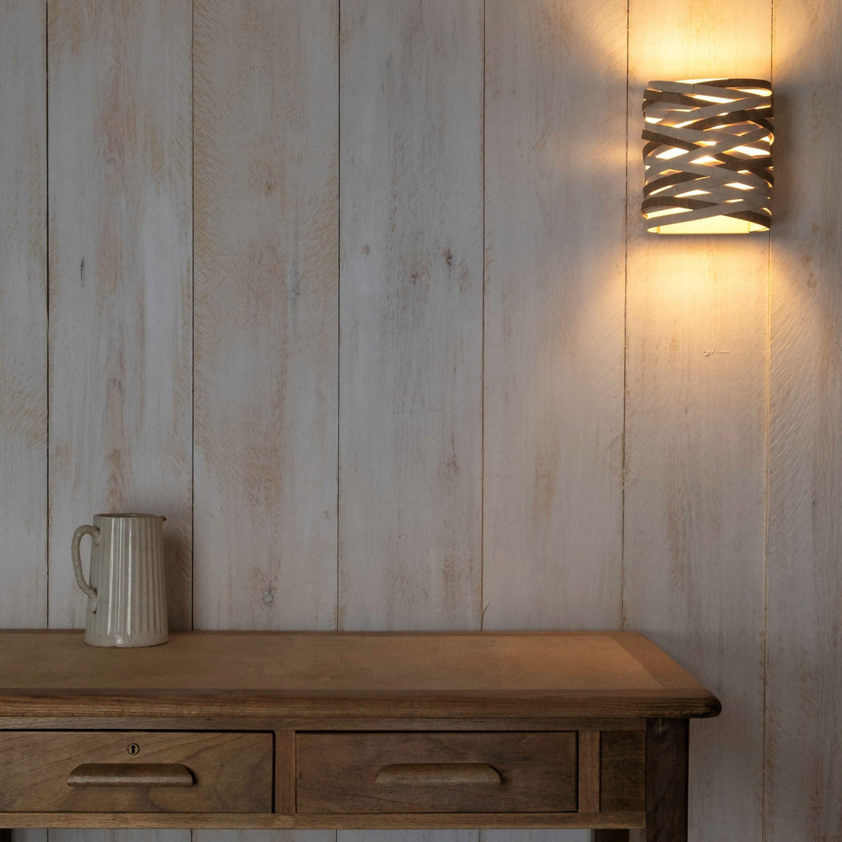 Wooden sideboard with ceramic jug under modern convolution wall light on rustic white wooden wall
